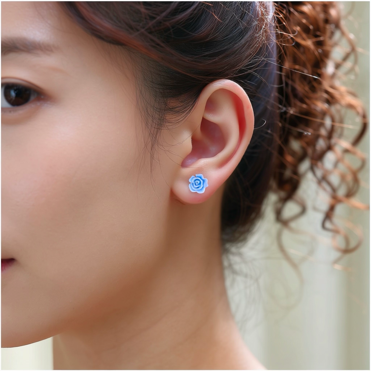 A close-up of a person's ear wearing a small pastel blue rose-shaped titanium stud earring.