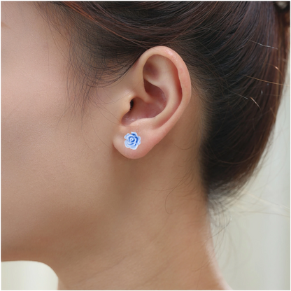 A close-up of a person's ear wearing a small pastel blue rose-shaped titanium stud earring.