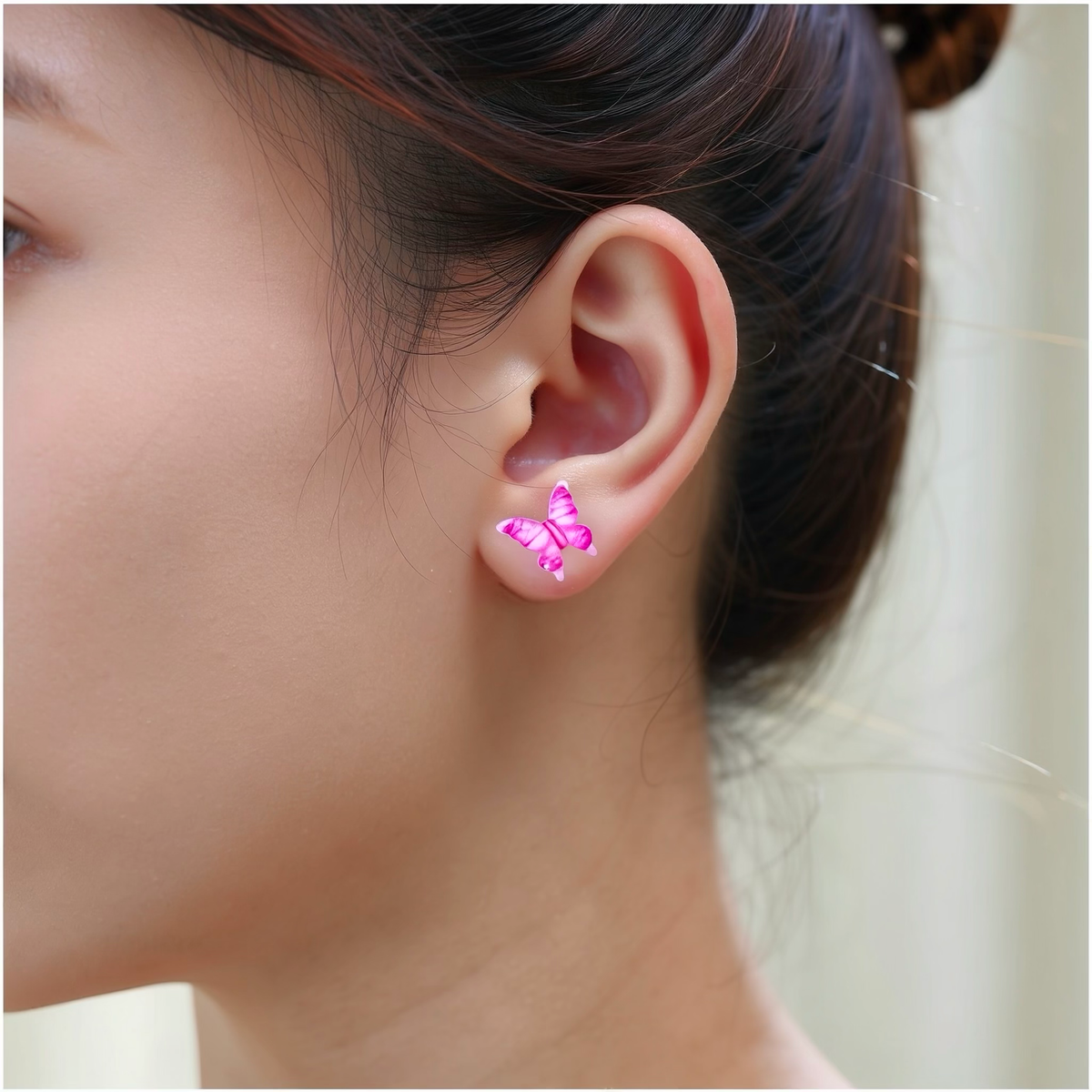A close-up of a person's ear wearing a small butterfly-shaped titanium stud earring in shade of pink, and clear.
