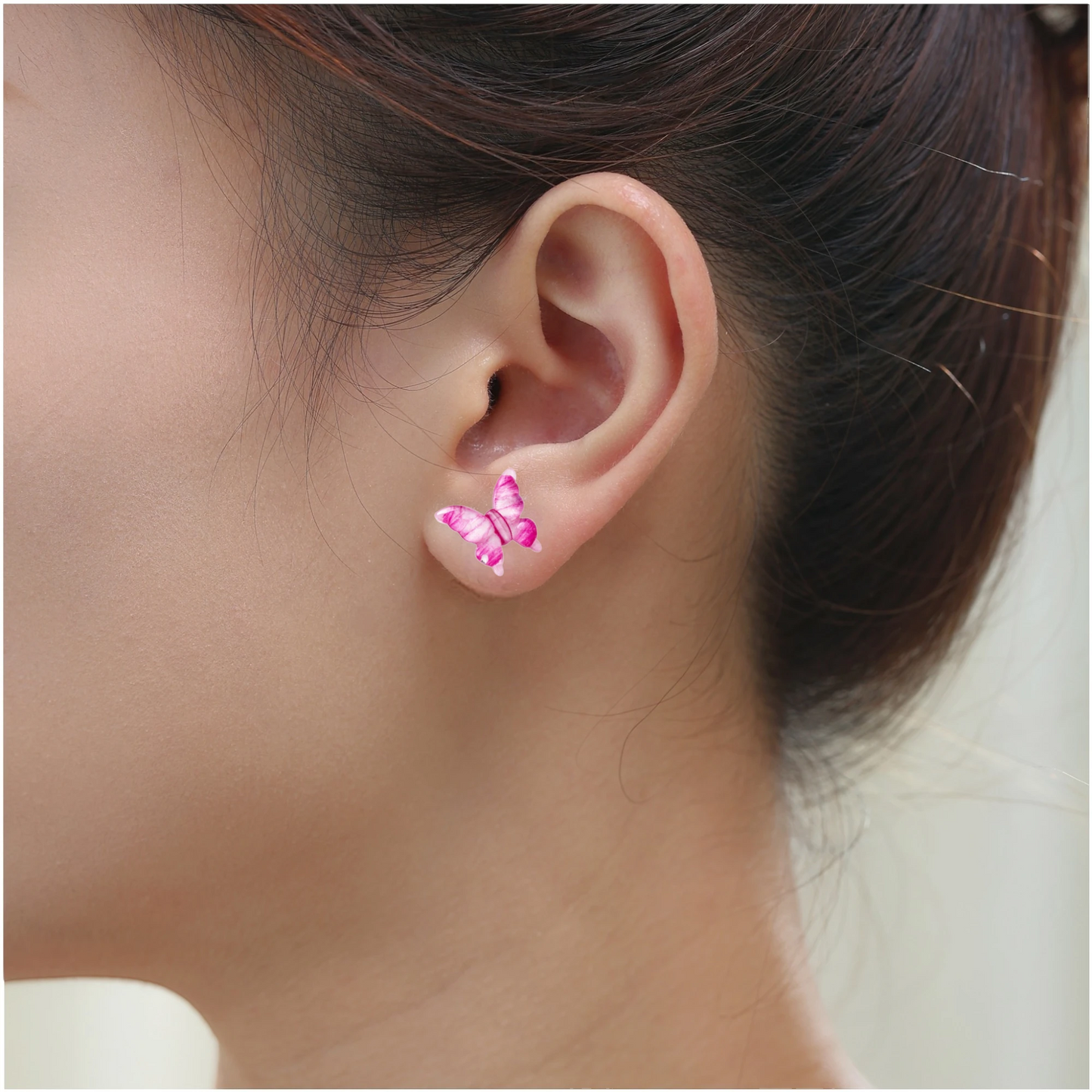 A close-up of a person's ear wearing a small butterfly-shaped titanium stud earring in shade of pink, and clear.
