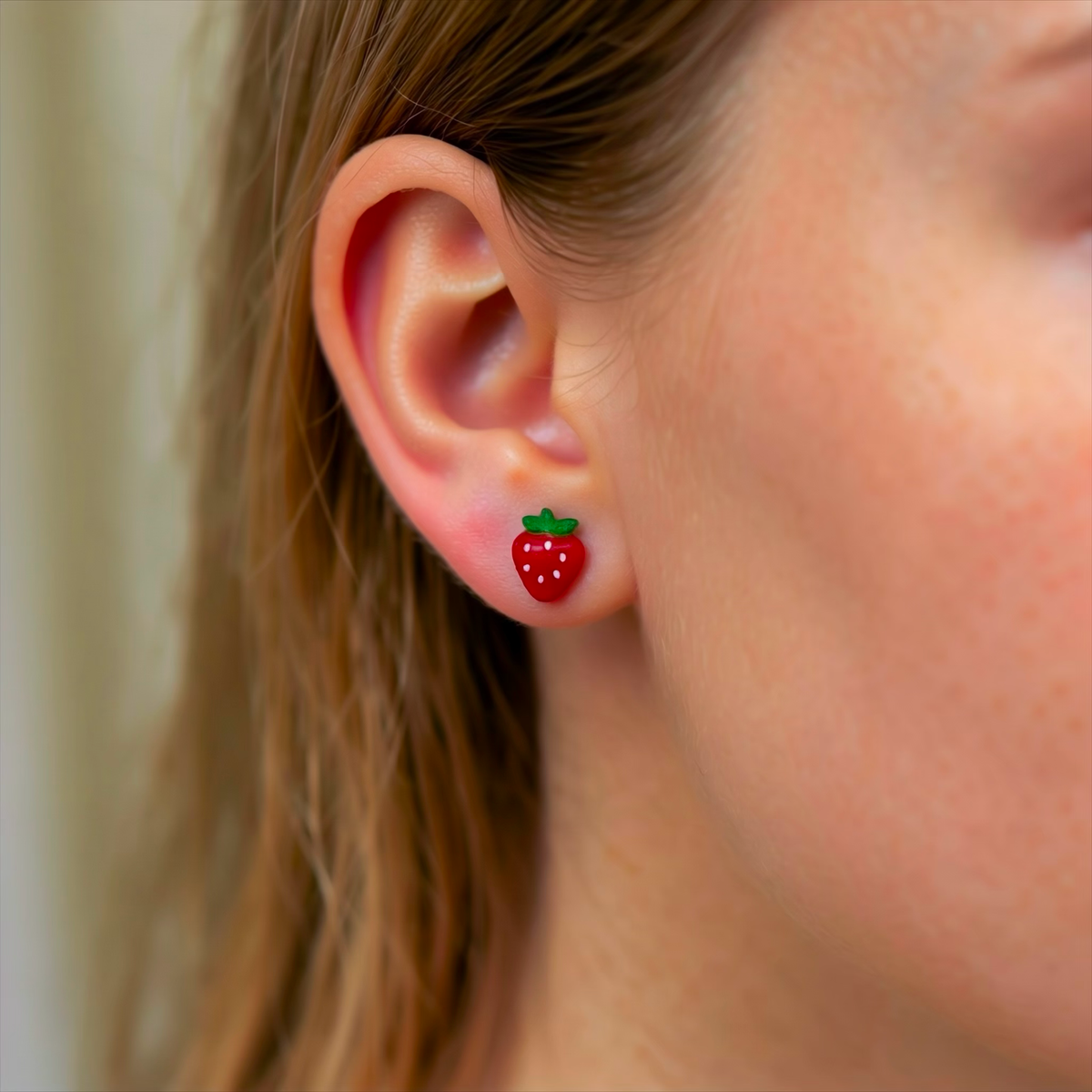 Small strawberry-shaped titanium stud earrings in shades of red and green on a young girl.