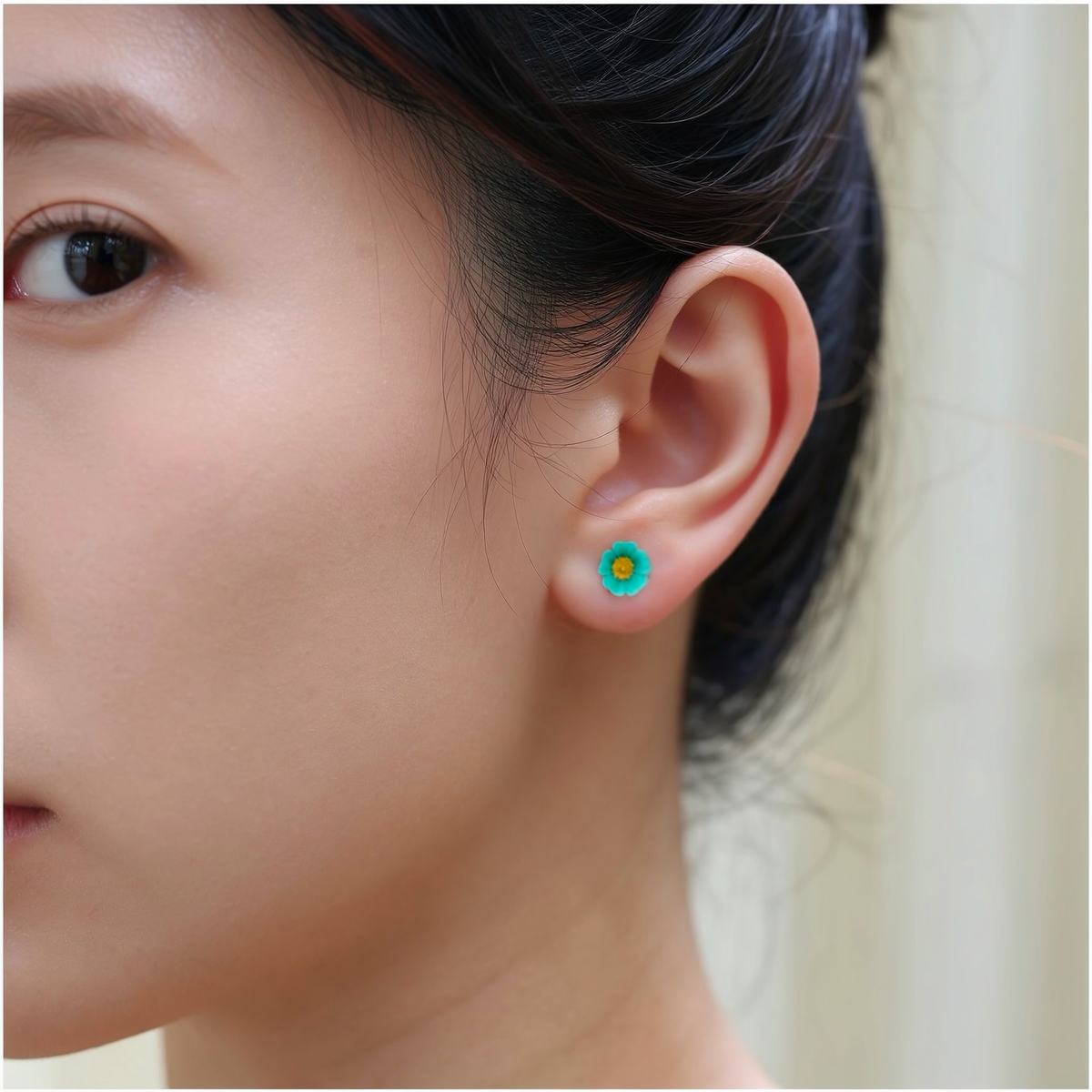 A close-up of a person's ear wearing a small bright blue and yellow marigold-shaped titanium stud earring.