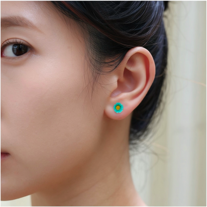 A close-up of a person's ear wearing a small bright blue and yellow marigold-shaped titanium stud earring.