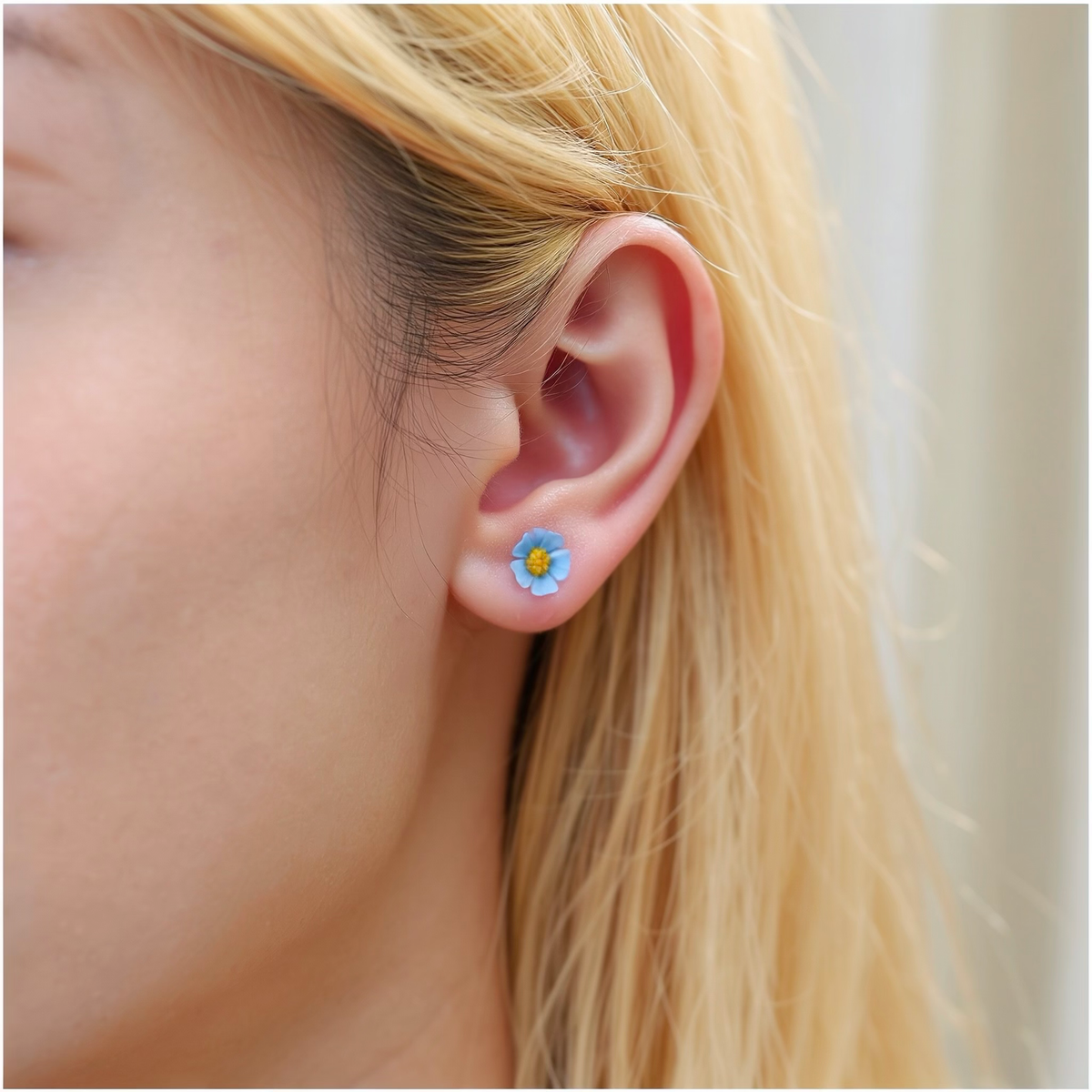 A close-up of a person's ear wearing a small pastel blue and yellow marigold-shaped titanium stud earring.