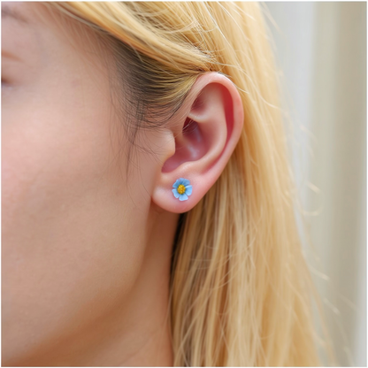 A close-up of a person's ear wearing a small pastel blue and yellow marigold-shaped titanium stud earring.