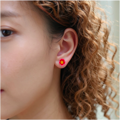 A close-up of a person's ear wearing a small pastel pink and yellow marigold-shaped titanium stud earring.