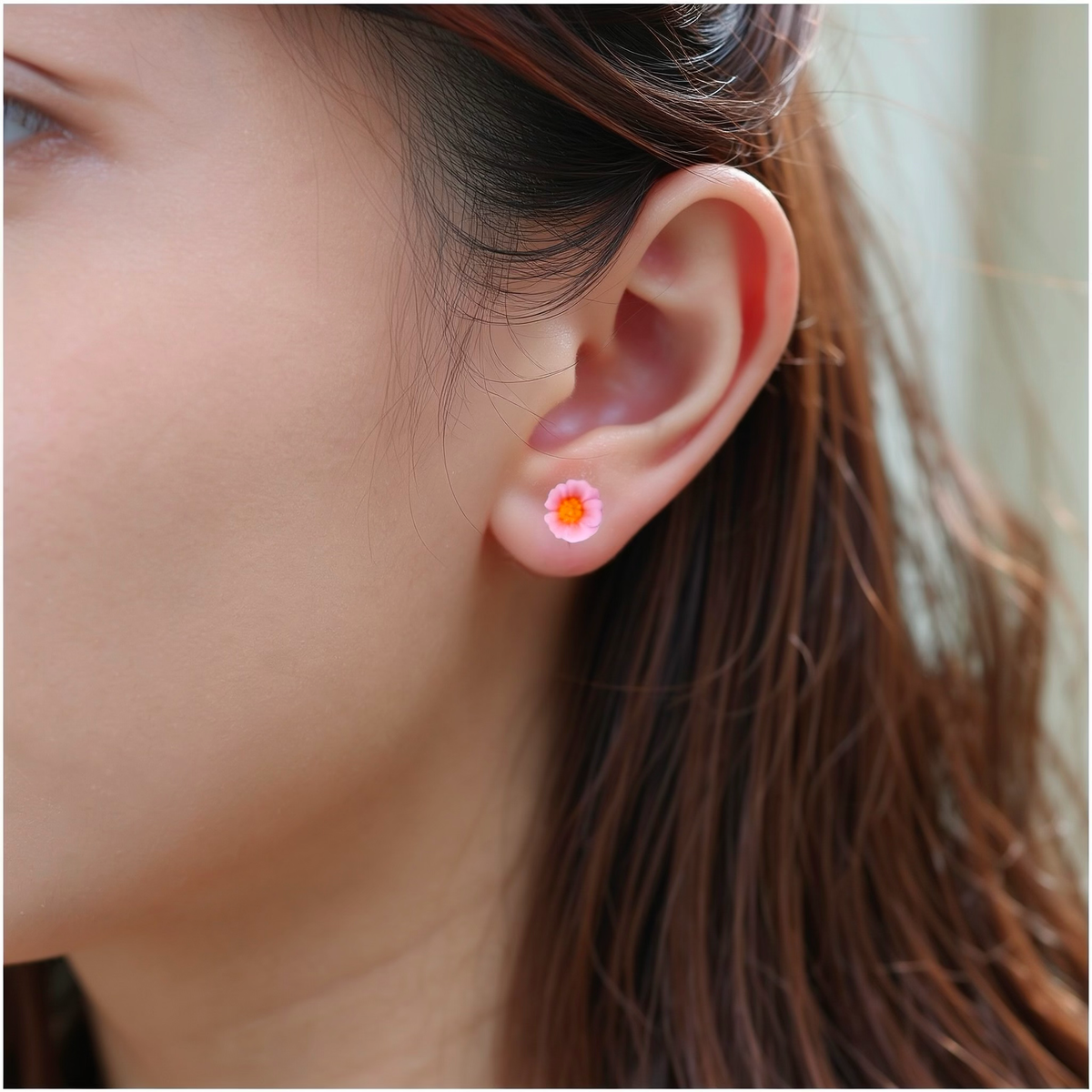 A close-up of a person's ear wearing a small light pink marigold-shaped titanium stud earring.