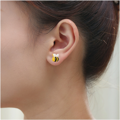 A woman wearing bee-themed stud earrings with yellow and black details and titanium post and backs, shown on a  white background.