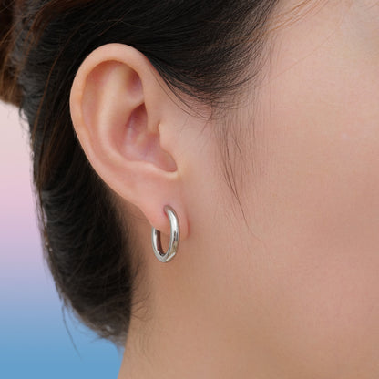 Close-up of an ear wearing a silver titanium hoop earring with a sky background
