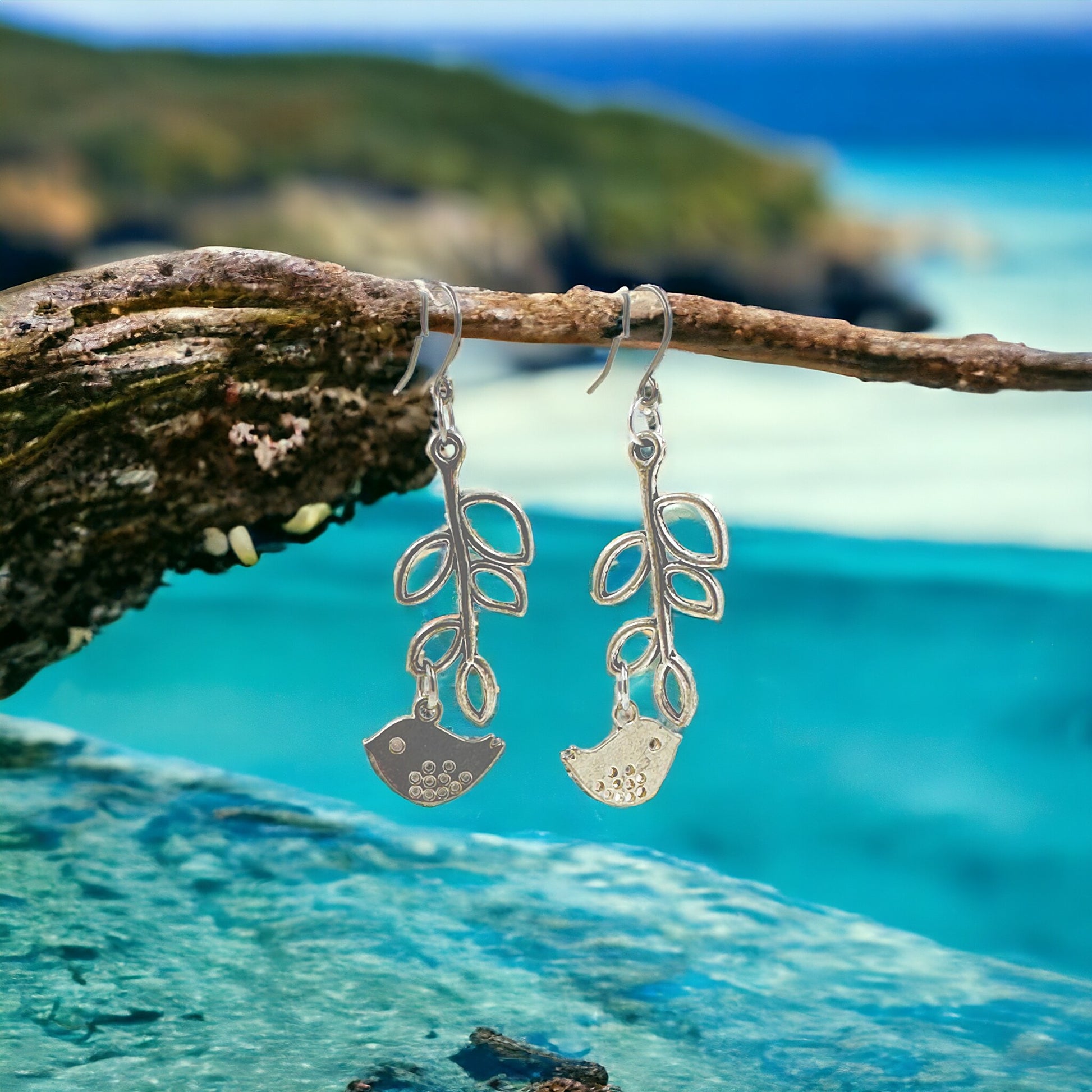 Songbird Charm earrings with a titanium hook on a ocean background blue