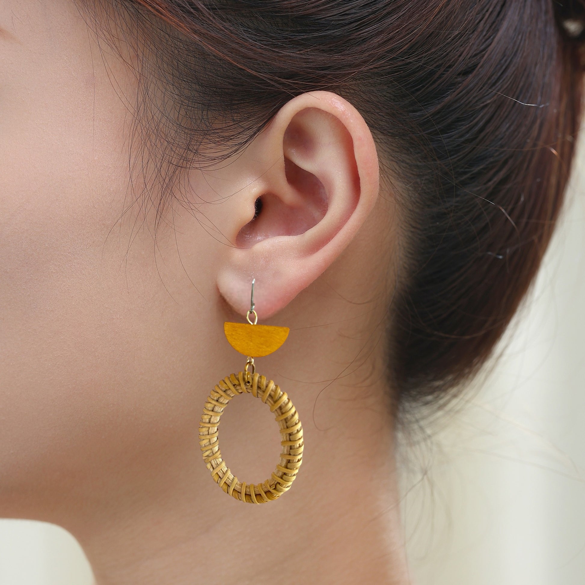 Bohemia style wicker and wood geometric earrings with titanium hook on a white young woman.