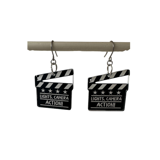 lights camera action titanium earrings on a white back ground