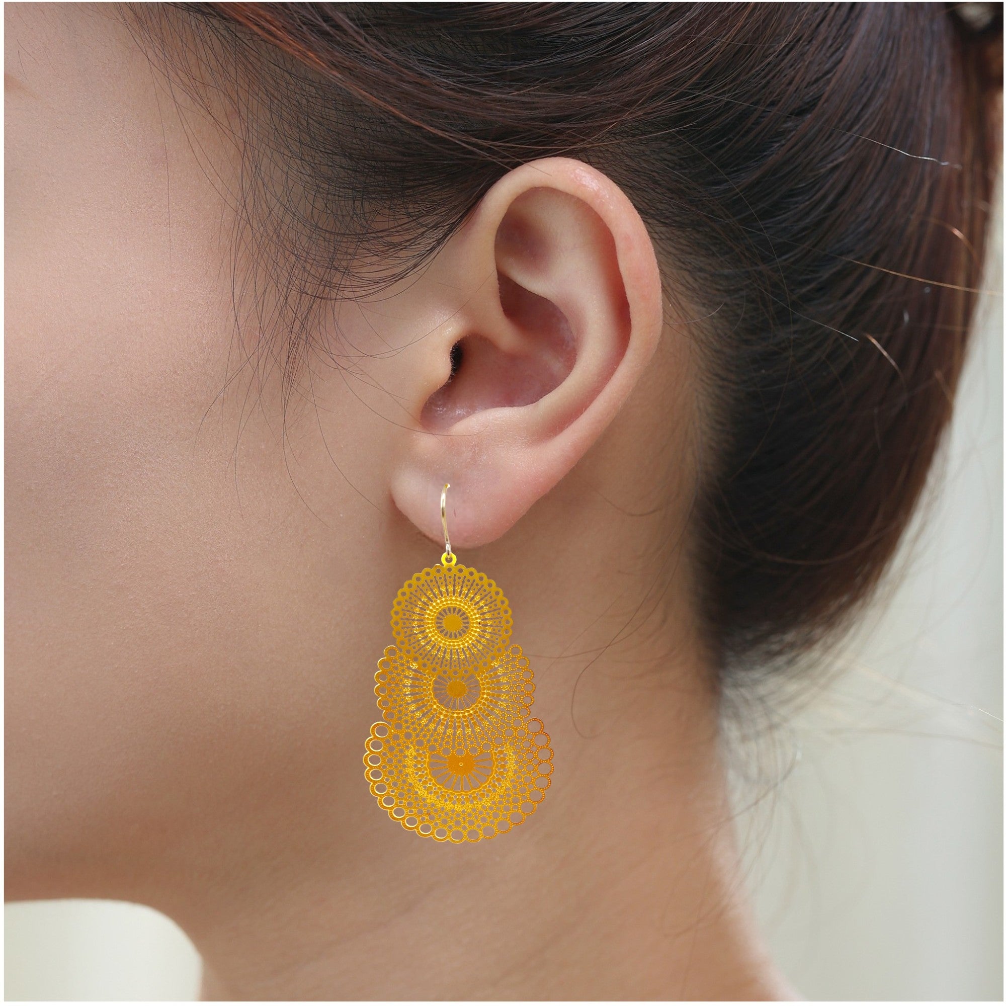 Triple gold disc drop earring with titanium hook. on a white young woman