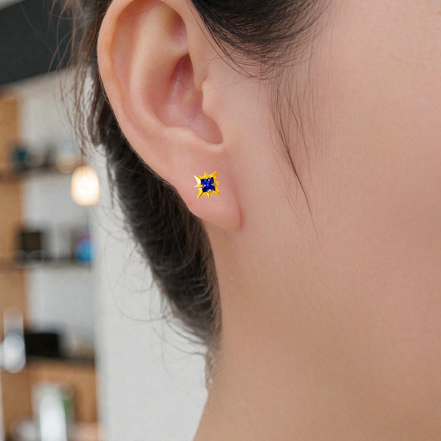 Close-up of an ear wearing a blue and gold titanium flat back threadless earring with a blurred background