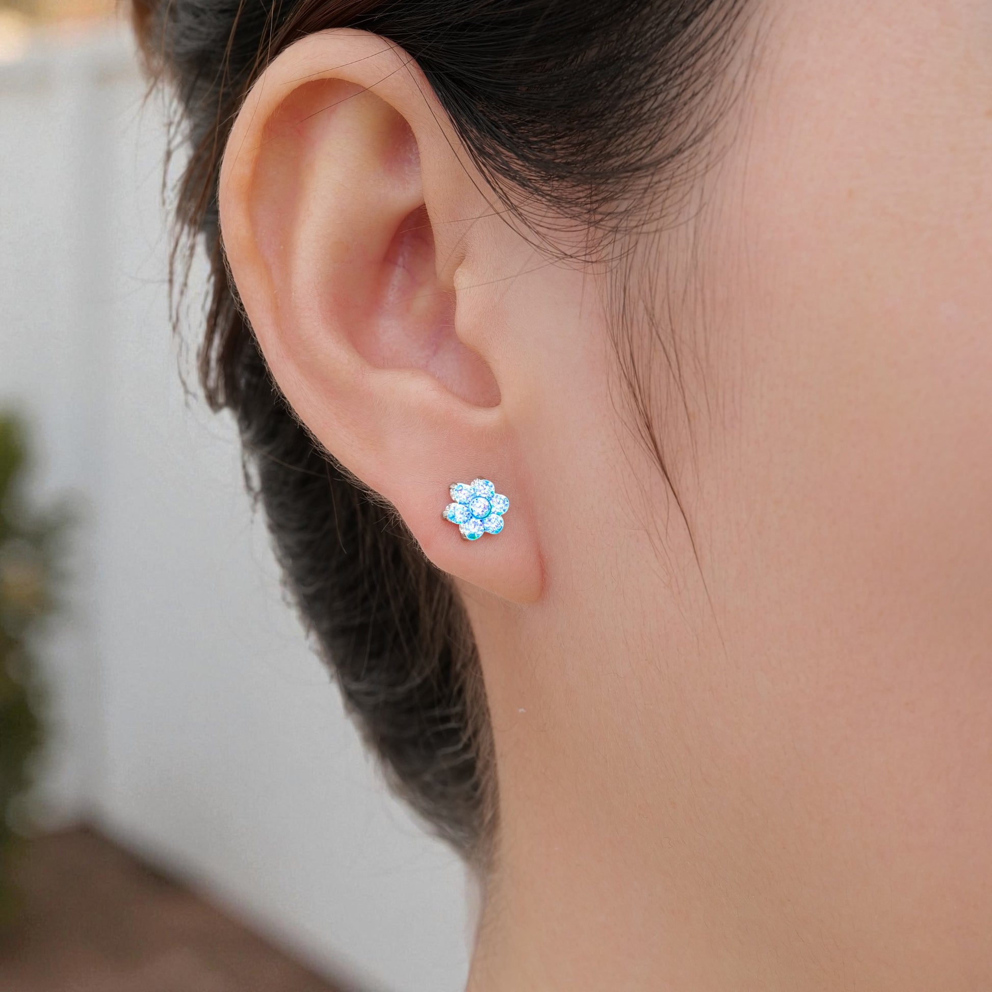 Close-up of an ear wearing a titanium floral aqua blue stud earring with a blurred background