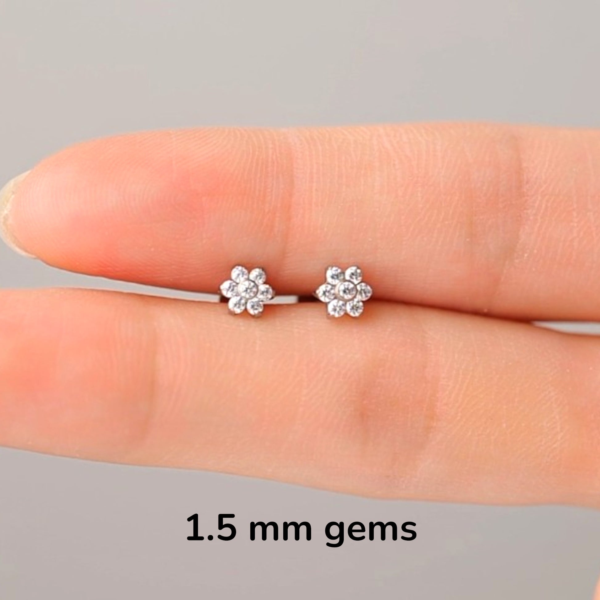 Titanium flat back threadless flower-shaped earrings with 1.5 mm gems on a hand