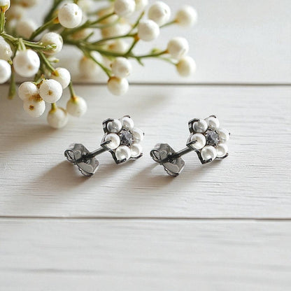 Pair of silver floral titanium earrings on a light wooden surface with white flowers in the background.