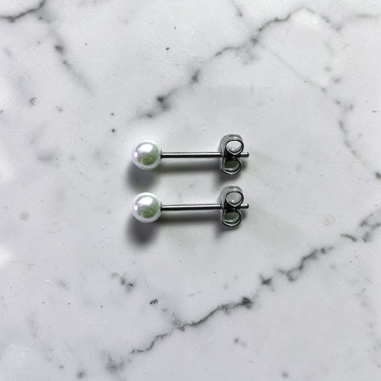 Pearl titanium stud earrings on a black box with a promotional text overlay on a marble background