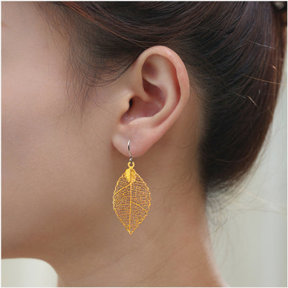 Small gold leaf earring with titanium hook on a woman