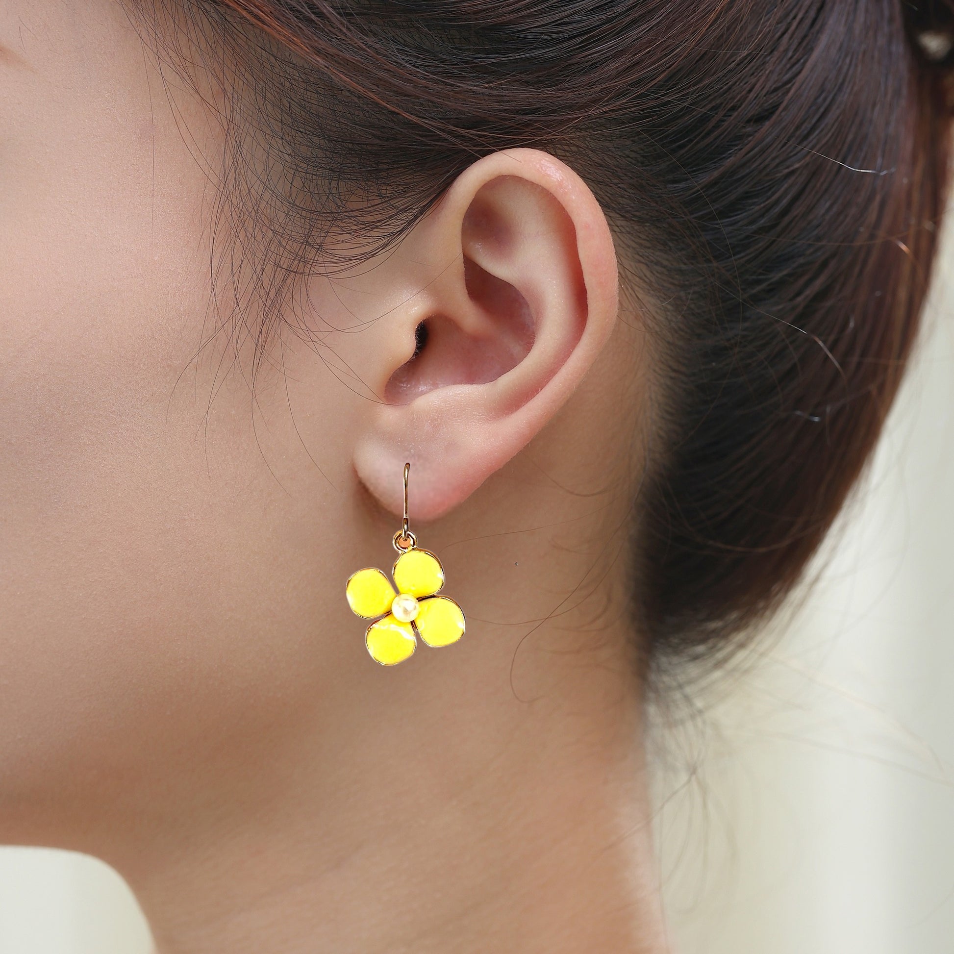 Forget Me Not earrings in yellow with a pearl in the center and a titanium hook on a white young woman