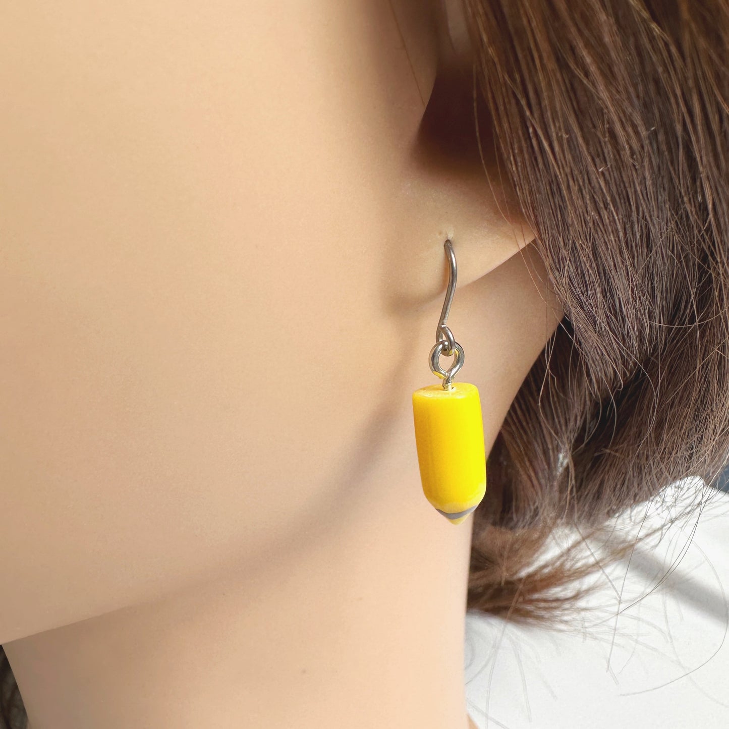 Pencil earrings with a titanium hook on a white young woman. yellow