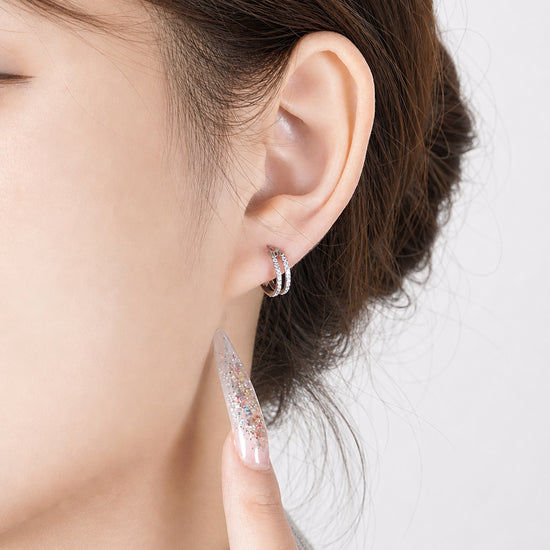 A close-up of a person's ear wearing a titanium small round-shaped hoop earring with diamond gems around both hoops.