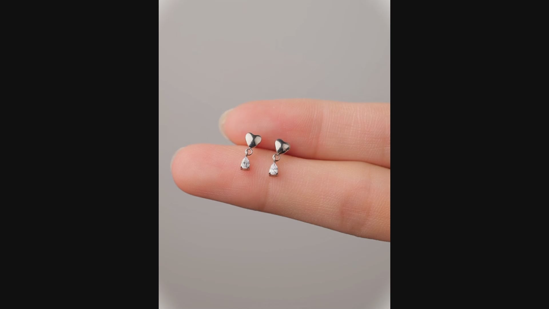titanium flat back 20 gauge heart studs with hanging gem on fingers and a woman
